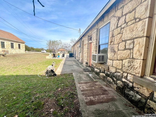 view of side of property featuring stone siding, cooling unit, and a lawn