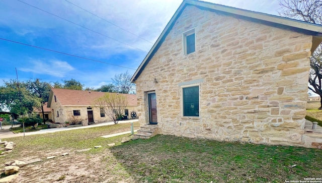 rear view of property with entry steps, stone siding, and a lawn