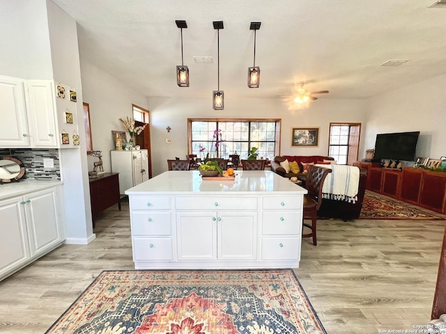 kitchen with a kitchen island, open floor plan, decorative light fixtures, light countertops, and white cabinetry