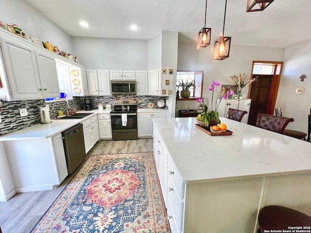 kitchen featuring stainless steel appliances, a sink, white cabinets, a center island, and pendant lighting