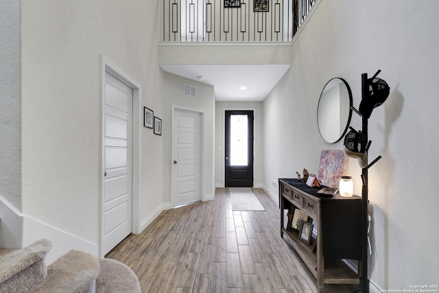 entryway featuring light wood finished floors, baseboards, visible vents, a towering ceiling, and stairs