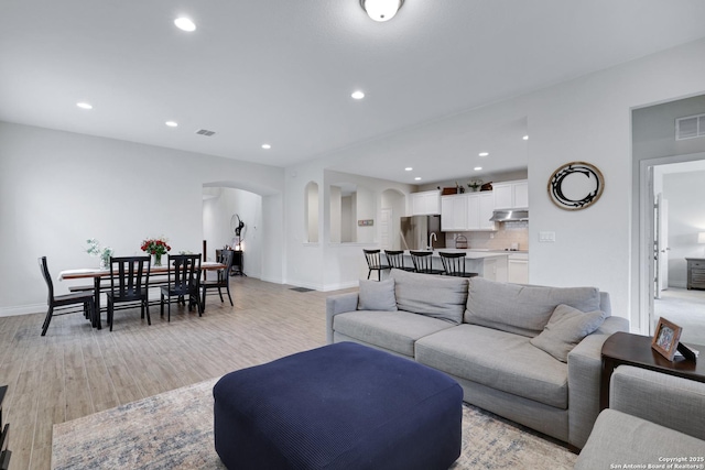 living area featuring arched walkways, light wood finished floors, recessed lighting, visible vents, and baseboards