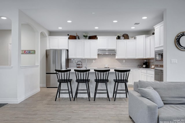 kitchen with stainless steel appliances, a kitchen island with sink, light countertops, and a breakfast bar