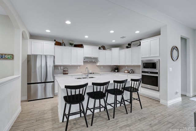 kitchen featuring under cabinet range hood, a sink, light countertops, appliances with stainless steel finishes, and a center island with sink