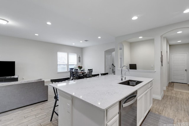 kitchen featuring arched walkways, open floor plan, a sink, a kitchen island with sink, and stainless steel dishwasher