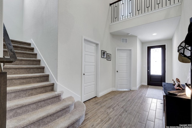 entrance foyer featuring visible vents, a towering ceiling, stairway, wood finished floors, and baseboards