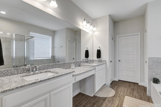 full bathroom featuring a stall shower, double vanity, a sink, and wood finished floors