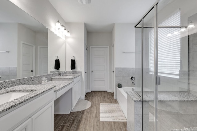 full bath with double vanity, a garden tub, a sink, and wood finished floors