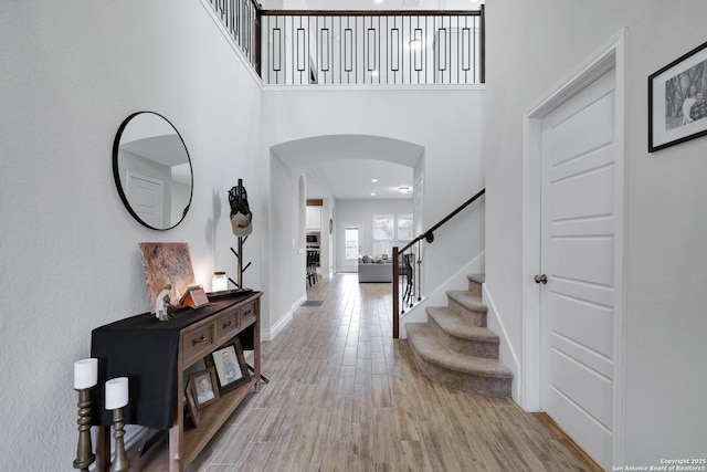 foyer with arched walkways, a high ceiling, baseboards, stairs, and light wood-type flooring