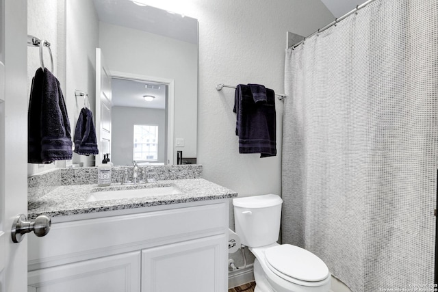 bathroom featuring toilet, a textured wall, and vanity