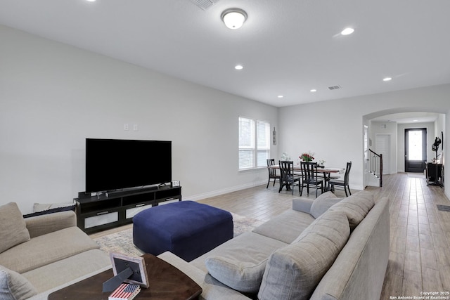 living area featuring baseboards, visible vents, arched walkways, light wood-style floors, and recessed lighting