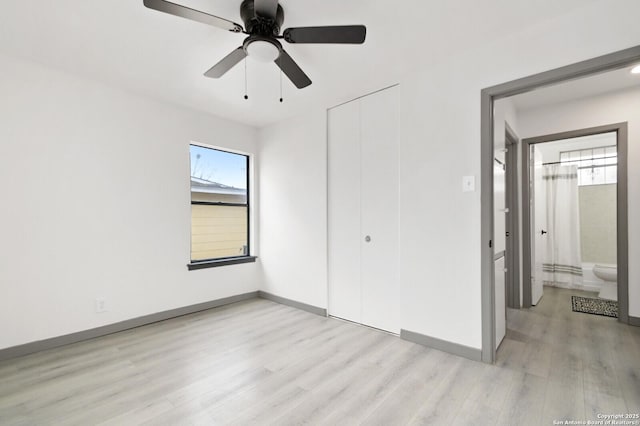 unfurnished bedroom featuring a closet, light wood-style flooring, baseboards, and ensuite bathroom