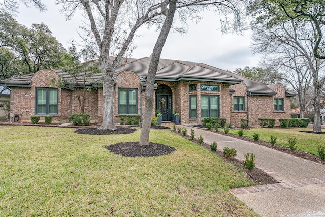 view of front facade with a front yard, a tile roof, and brick siding