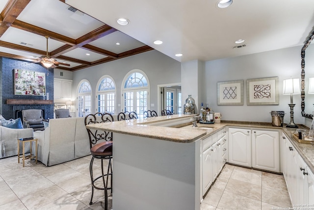 kitchen with a breakfast bar area, a brick fireplace, open floor plan, white cabinets, and coffered ceiling