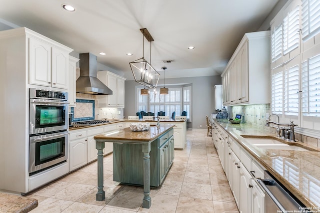 kitchen featuring decorative light fixtures, wall chimney range hood, white cabinetry, and a center island