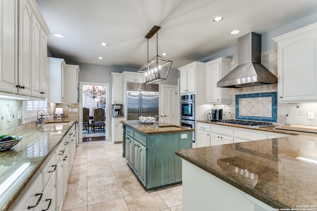 kitchen featuring wall chimney range hood, a kitchen island, white cabinetry, and stainless steel appliances