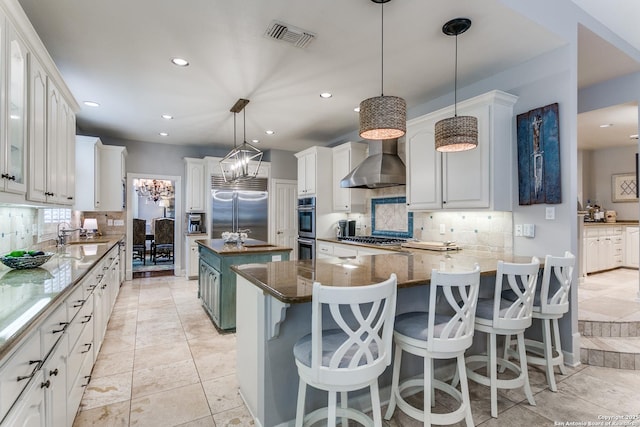 kitchen with wall chimney exhaust hood, appliances with stainless steel finishes, white cabinetry, and a center island