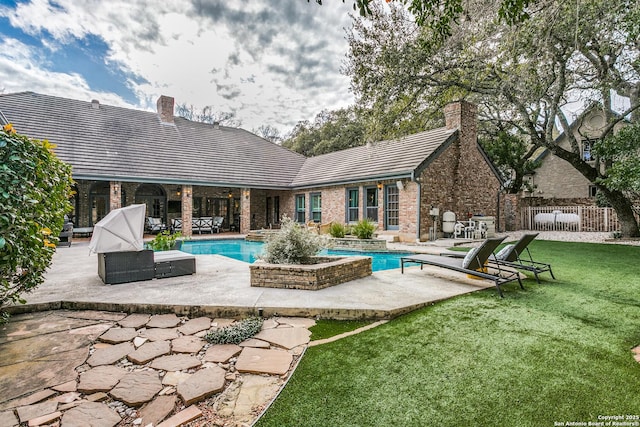 back of property featuring brick siding, a chimney, a patio area, and an outdoor pool