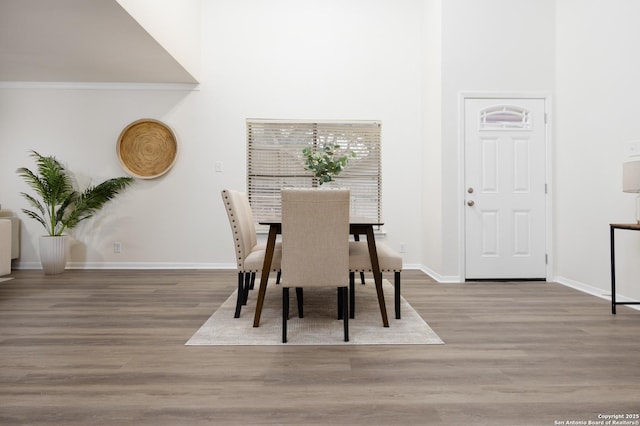 dining room with light wood-type flooring, a towering ceiling, and baseboards