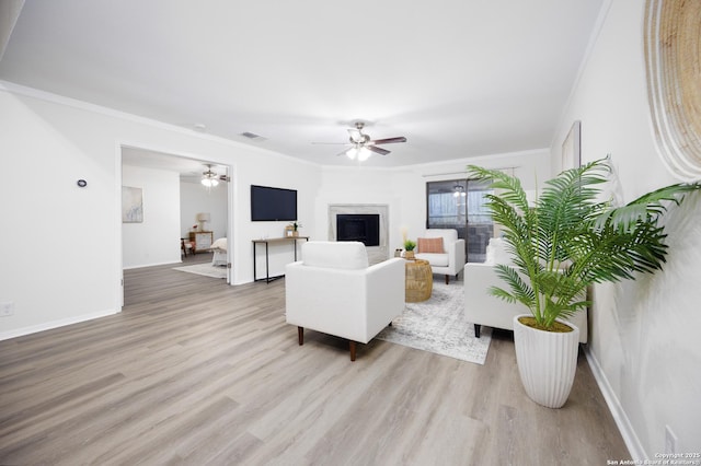 living area with ceiling fan, light wood-style flooring, a fireplace, baseboards, and crown molding