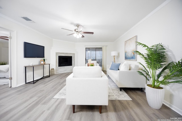 living room featuring visible vents, a ceiling fan, light wood-style flooring, ornamental molding, and a high end fireplace