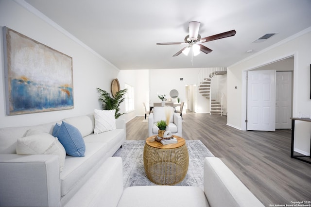 living area featuring crown molding, visible vents, ceiling fan, wood finished floors, and stairs