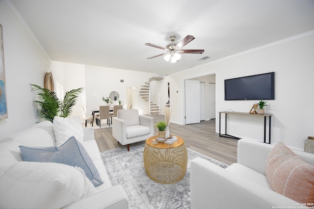 living area featuring ornamental molding, light wood-type flooring, visible vents, and stairway