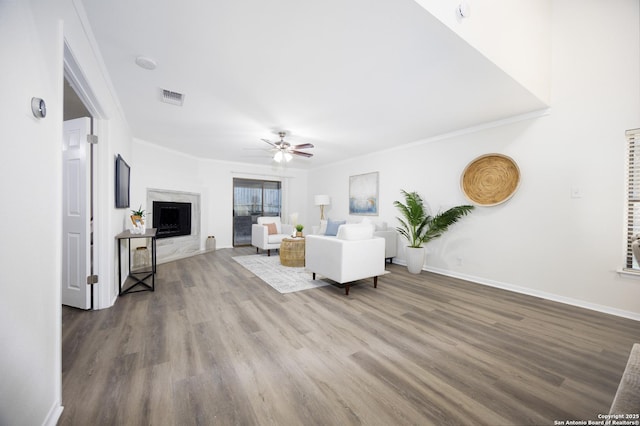 living room with crown molding, a fireplace, visible vents, a ceiling fan, and wood finished floors