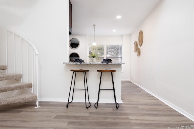 kitchen featuring a peninsula, light wood-type flooring, a kitchen bar, and decorative light fixtures