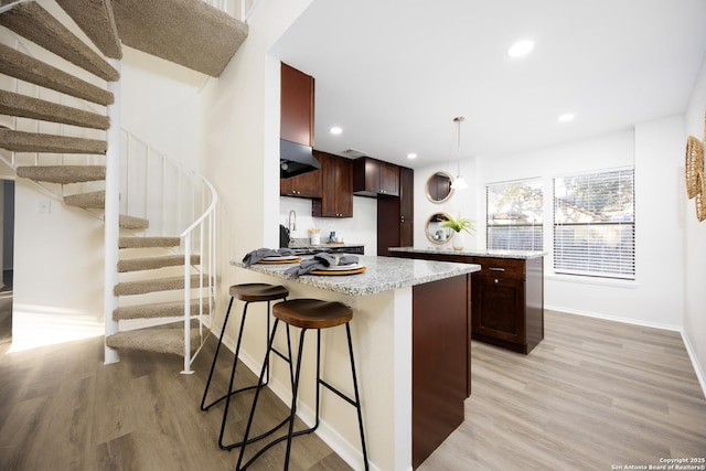 kitchen featuring a peninsula, under cabinet range hood, light wood-style floors, and decorative light fixtures