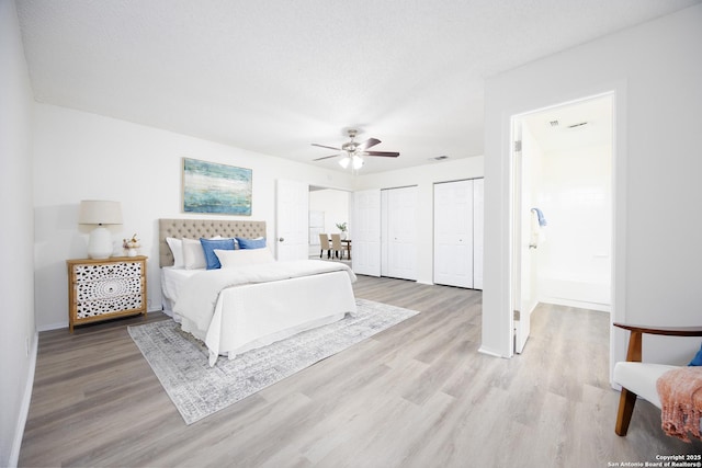 bedroom featuring a textured ceiling, wood finished floors, visible vents, baseboards, and multiple closets