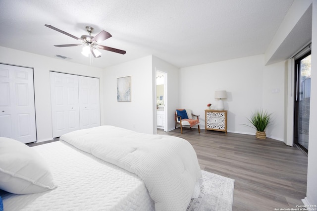 bedroom featuring visible vents, ceiling fan, wood finished floors, a textured ceiling, and multiple closets