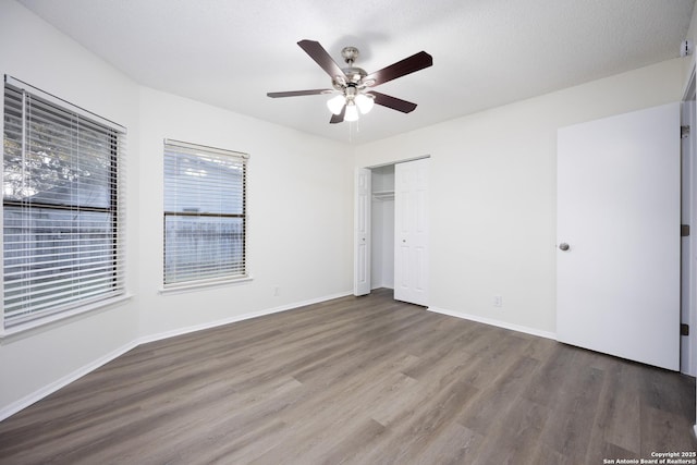 unfurnished bedroom with a textured ceiling, a ceiling fan, baseboards, a closet, and dark wood finished floors