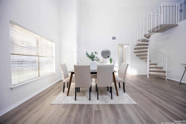 dining room with a high ceiling, wood finished floors, visible vents, baseboards, and stairway