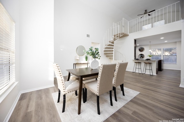 dining space with a high ceiling, stairway, baseboards, and wood finished floors