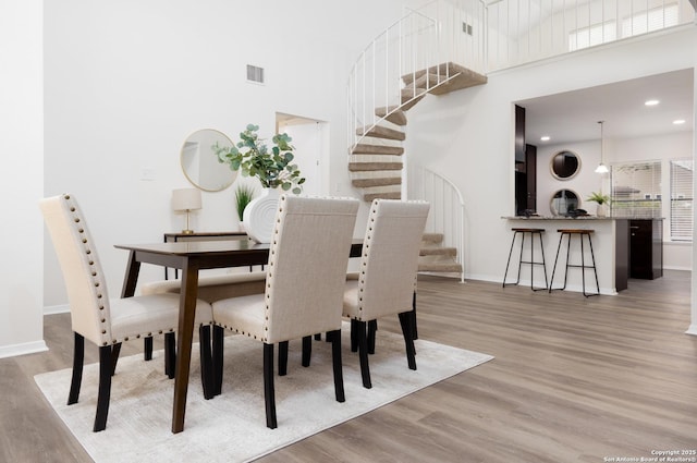 dining space with a towering ceiling, light wood-style flooring, stairway, and baseboards