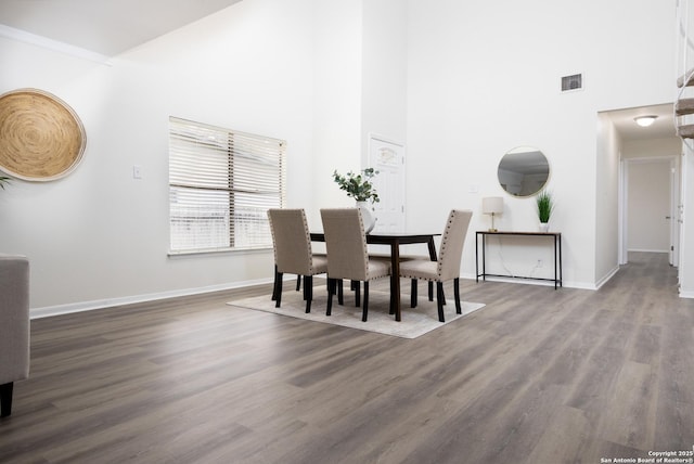 dining area featuring a towering ceiling, wood finished floors, visible vents, and baseboards