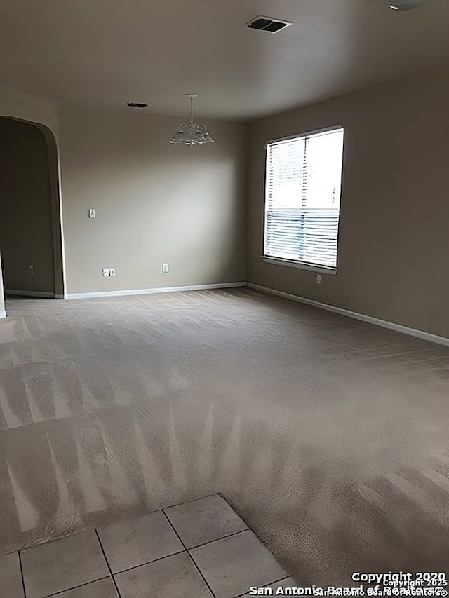 spare room featuring arched walkways, visible vents, and light colored carpet