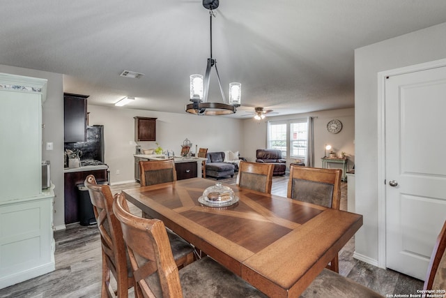 dining area featuring ceiling fan with notable chandelier, light wood-type flooring, visible vents, and baseboards