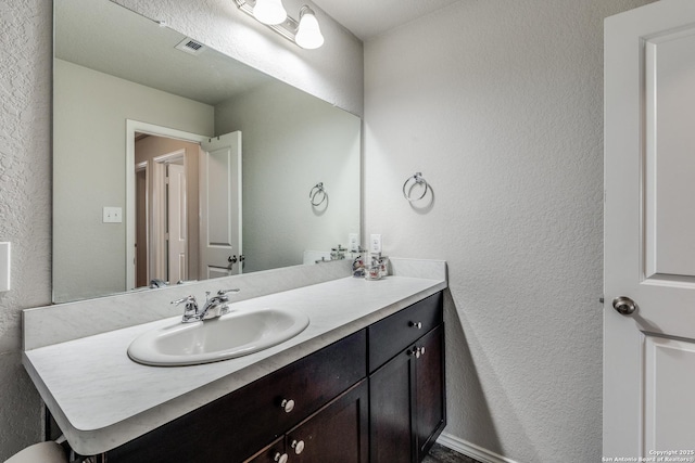 bathroom featuring a textured wall, vanity, and visible vents