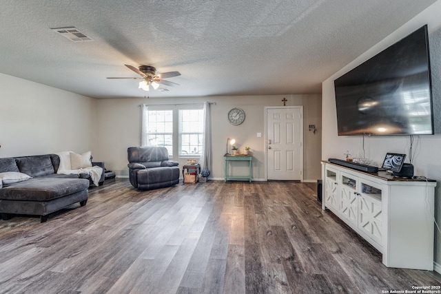 living room with dark wood-style floors, ceiling fan, visible vents, and a textured ceiling