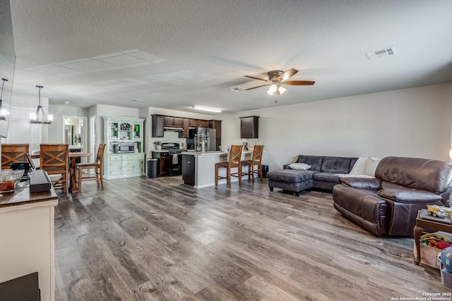 living area with ceiling fan with notable chandelier, visible vents, a textured ceiling, and wood finished floors