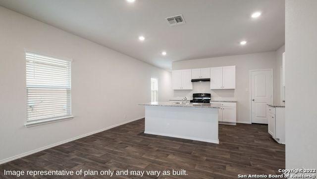 kitchen with dark wood-type flooring, visible vents, white cabinets, range, and an island with sink