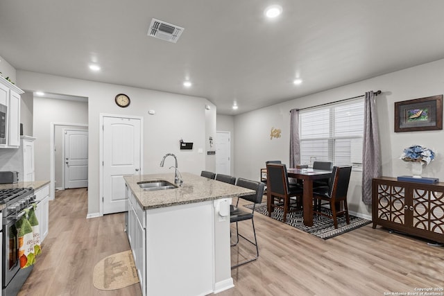 kitchen featuring a sink, a kitchen breakfast bar, white cabinets, an island with sink, and gas range