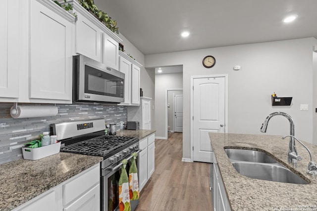 kitchen with stone countertops, white cabinetry, stainless steel appliances, and a sink