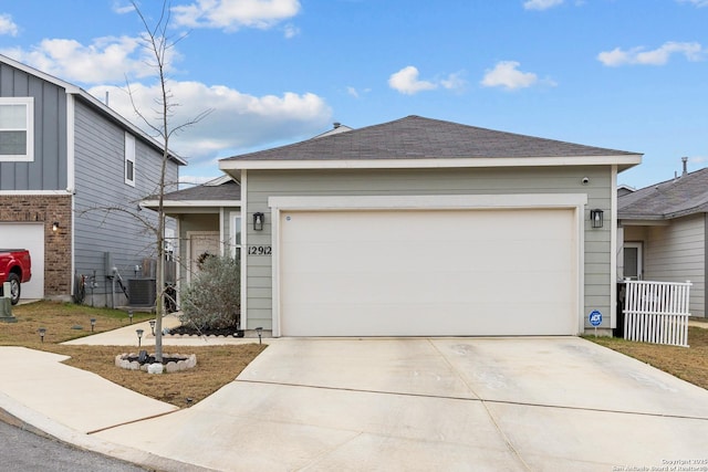 ranch-style house featuring concrete driveway, central AC, an attached garage, and roof with shingles