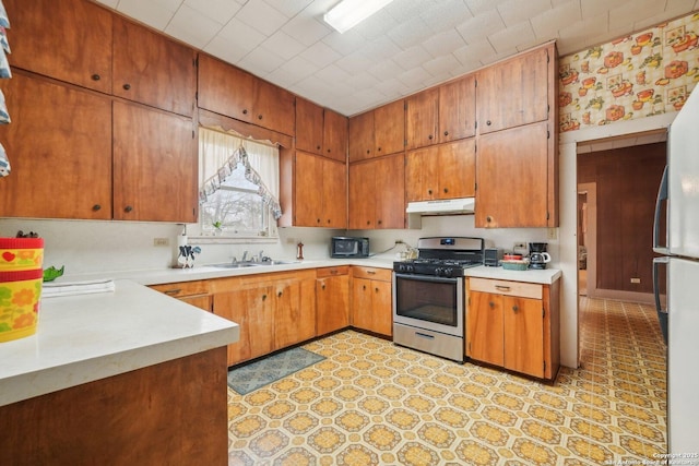 kitchen with stainless steel range with gas cooktop, light countertops, freestanding refrigerator, a sink, and under cabinet range hood