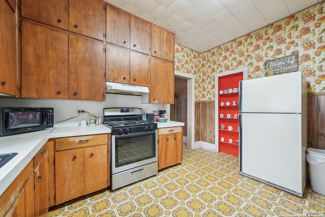 kitchen featuring black microwave, under cabinet range hood, stainless steel range with gas cooktop, freestanding refrigerator, and wallpapered walls