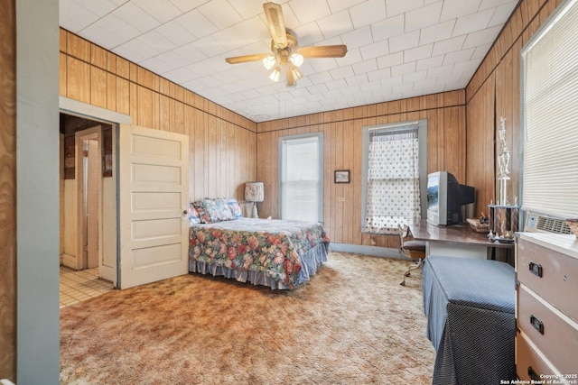 bedroom featuring light carpet, wood walls, and a ceiling fan