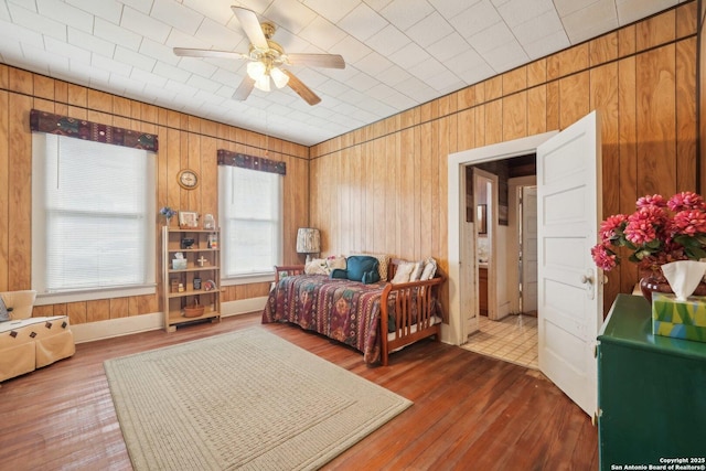 bedroom featuring ceiling fan, dark wood-type flooring, and wooden walls